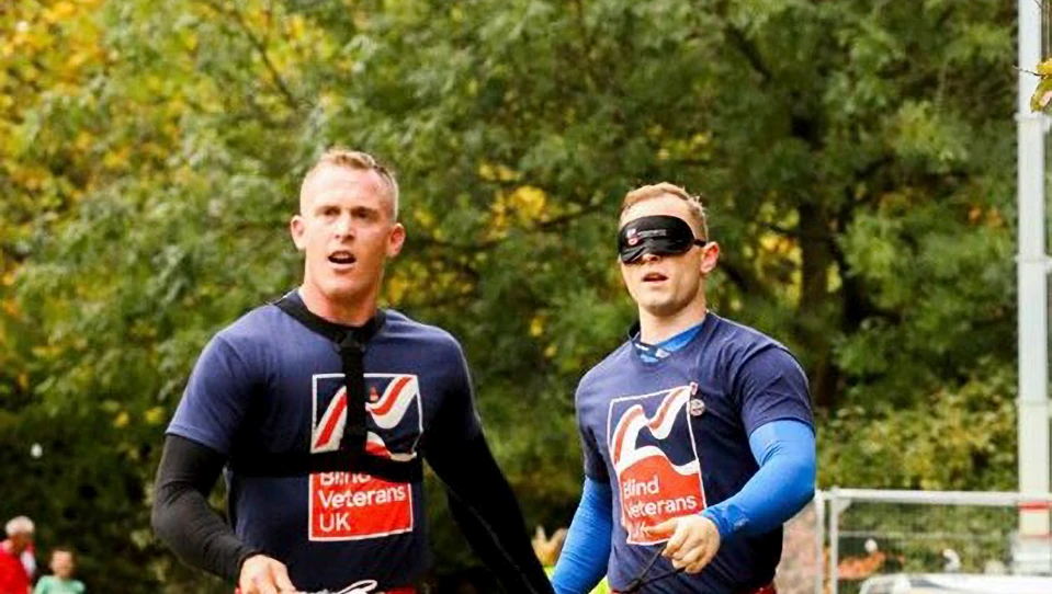 Charity supporter Nephi, running blindfolded, holding a piece of rope connected to his guide, who runs slightly ahead of him.