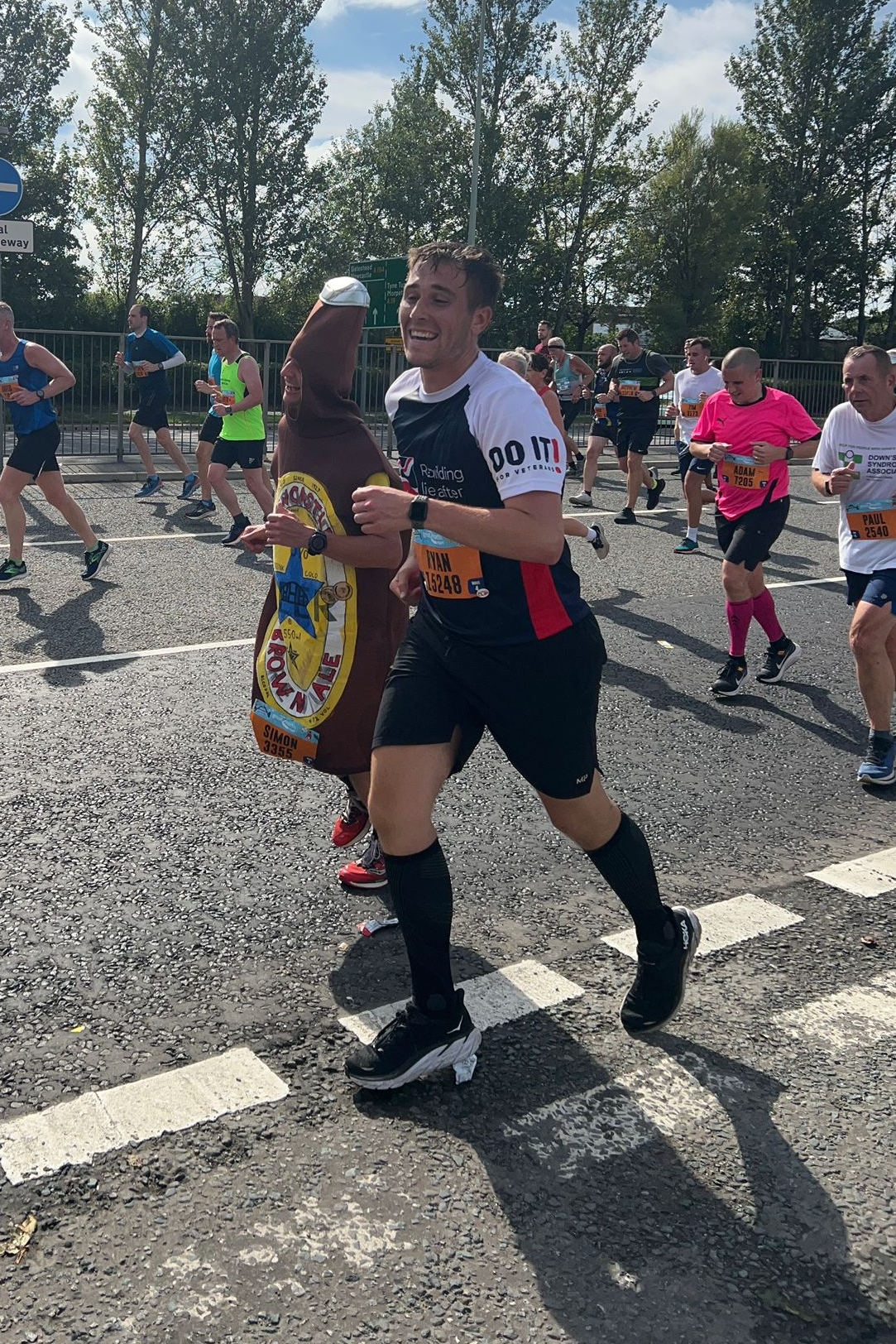 Ryan wearing a Blind Veterans UK t-shirt and running next to a man in a beer bottle costume