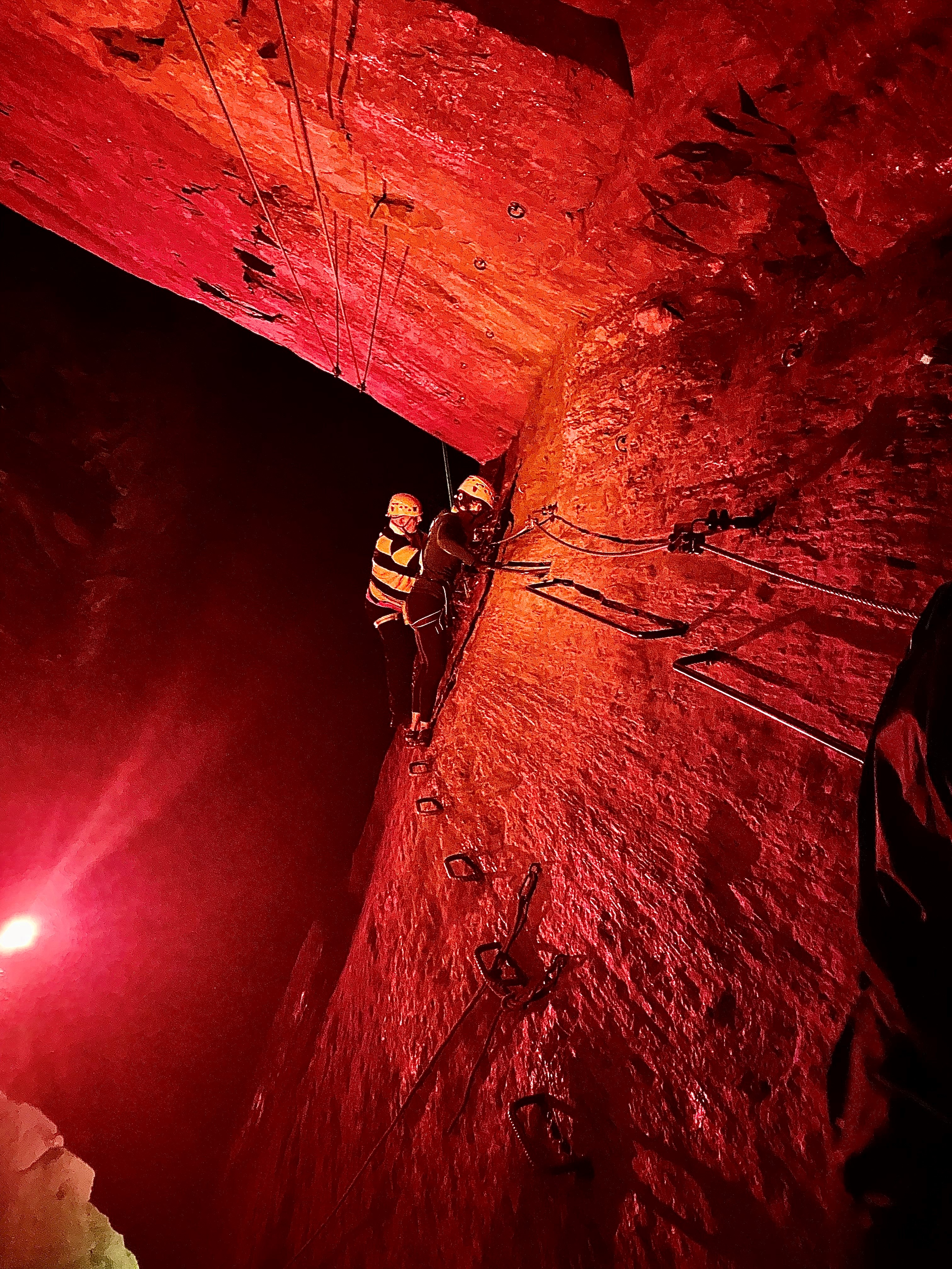 Blind veteran Jules wearing safety gear and a zip-wire harness as he edges along a cavern wall, using footholds and hand barriers
