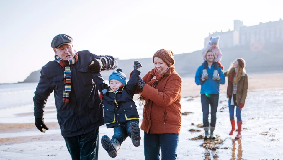 Two happy couples walking along the beach, both with a child in hand