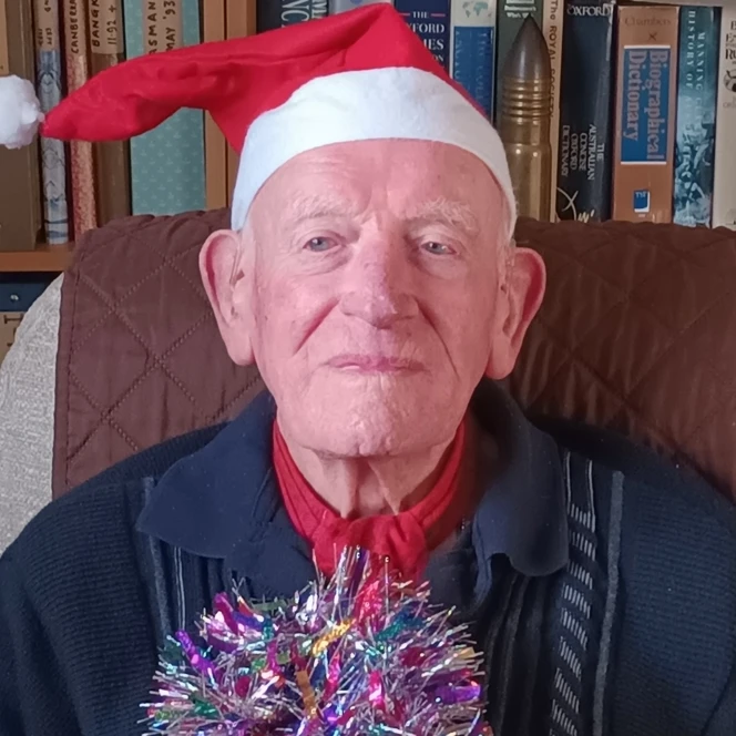 Mike smiling, wearing a Santa hat and holding some colourful tinsel.