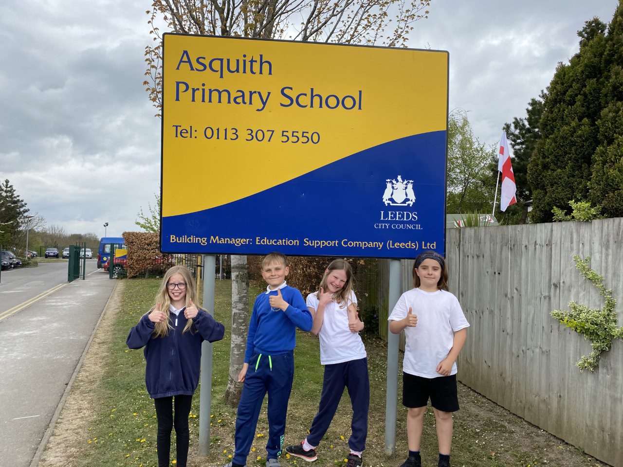 Four primary school children giving a thumbs up in front of the Asquith Primary School sign
