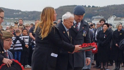 Arthur and Steph stand back and take in the wreaths already laid at the Llandudno War Memorial. Steph is holding a wreath ready to help Arthur to lay it