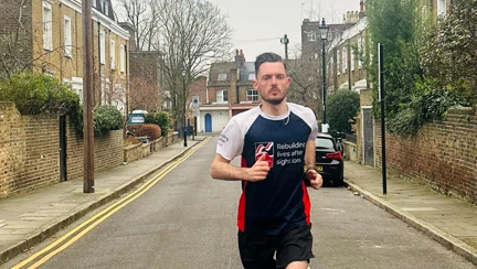 Rob running along the middle of a residential road in his Blind Veterans UK T-shirt