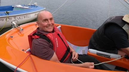 Blind veteran, Simon, smiling as he sits in an orange sailboat on the water