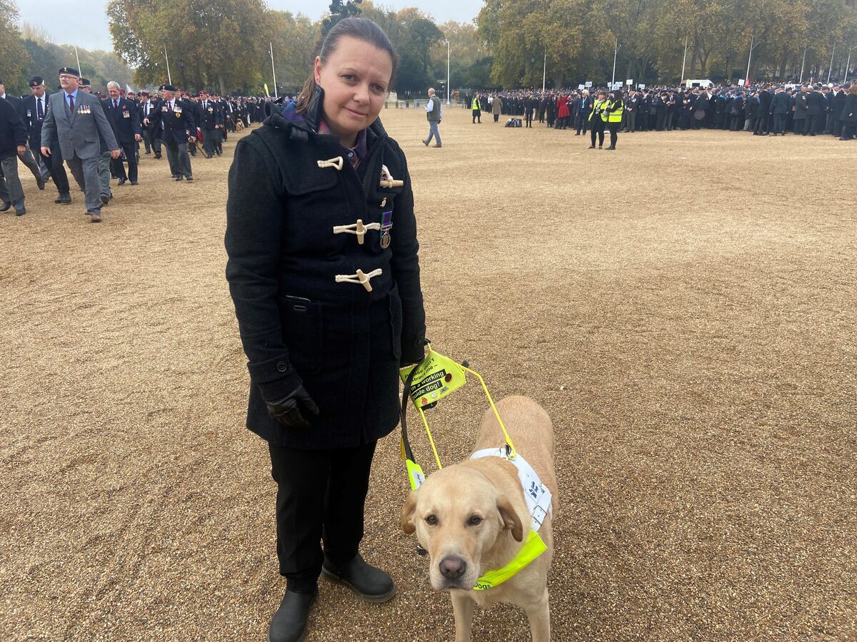A picture of Kelly with Archie at Horseguard's Parade. Kelly is wearing a smart black coat and is holding on to her guide dog Archie with his yellow harness
