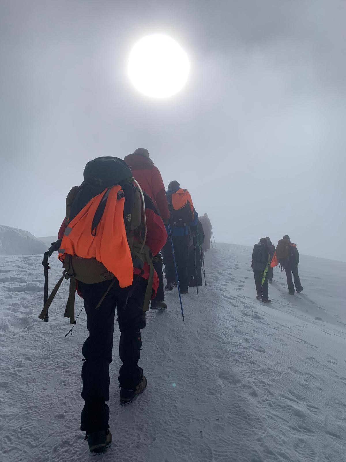 The group of climbers use walking poles to help them through the snow and ice near the top of Mount Kilimanjaro