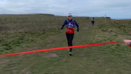 Rachel smiling as she runs towards a red finish line being held by her family