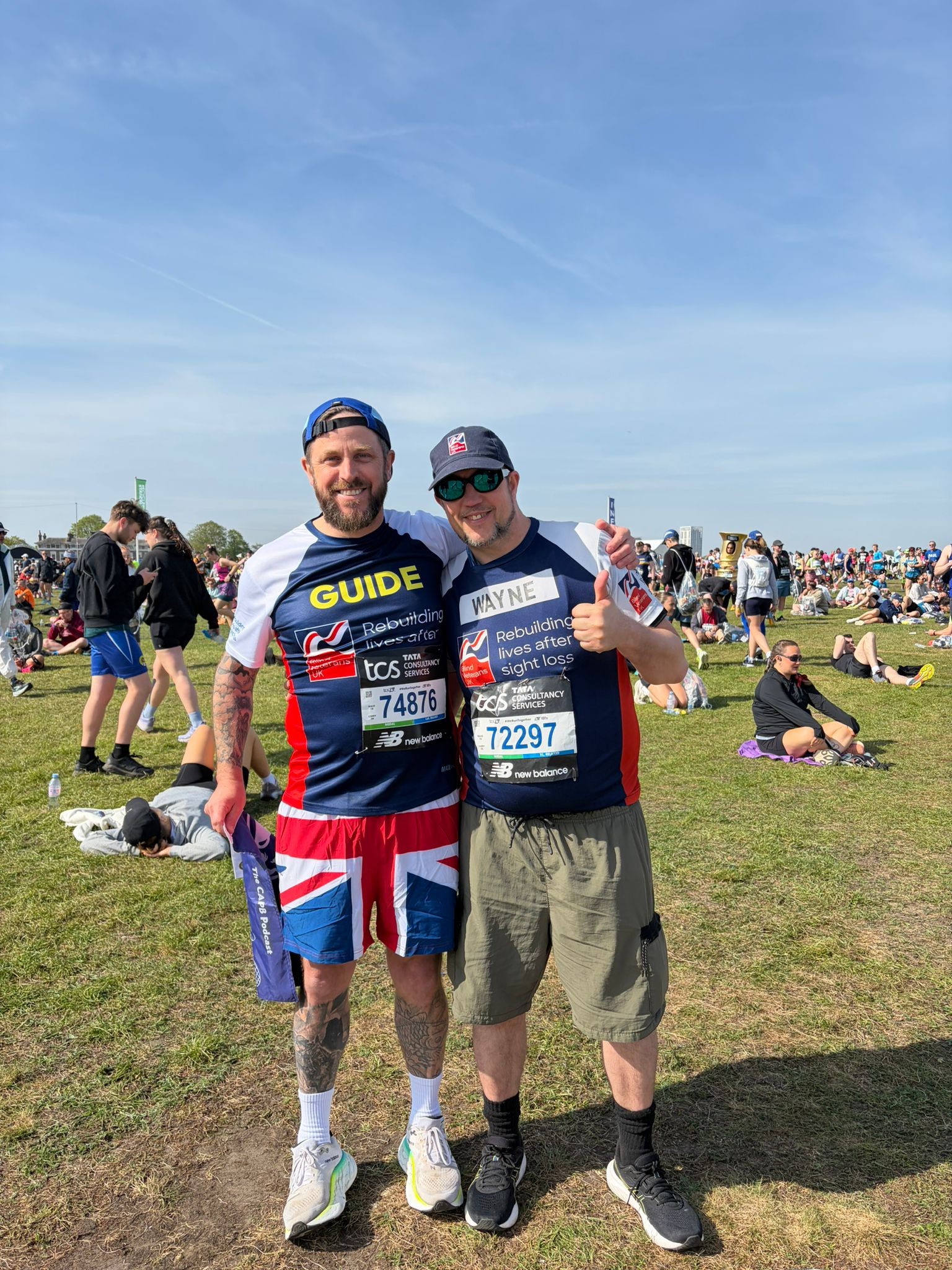 Wayne and Matt are stood together smiling ahead of the start of the marathon. Both are wearing Blind Veterans UK t-shirts and Matt is wearing a bold pair of Union Jack shorts