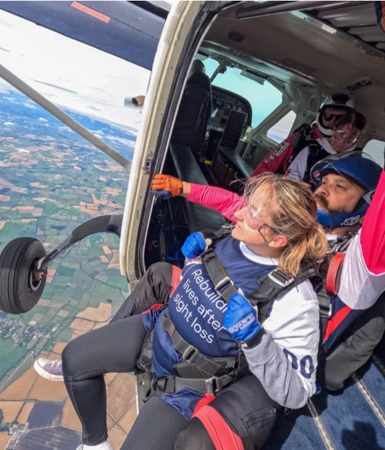 Olivia, attached to her colleague Jim, hang out of the plane door at 14,000 feet about to jump