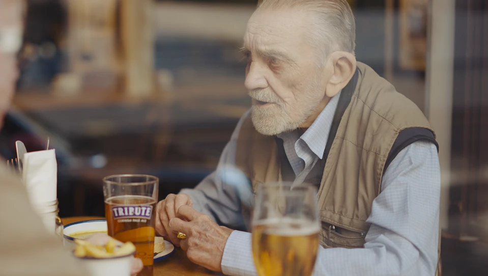 Blind veteran Ken and volunteer Liam sitting down, chatting in a pub, with drinks and food on the table