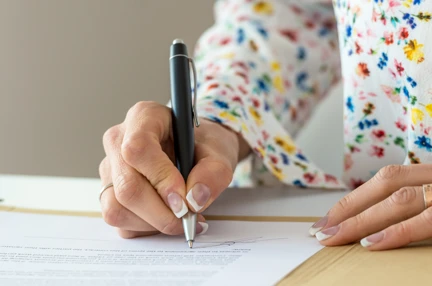 A woman sat at a desk using a pen to write on documents.