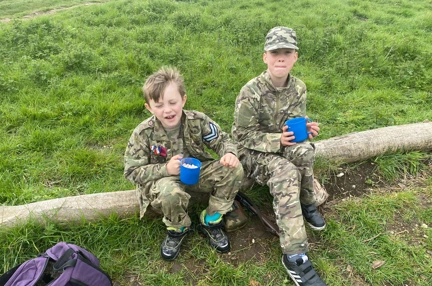 Two boys sat on a log wearing camouflage clothing