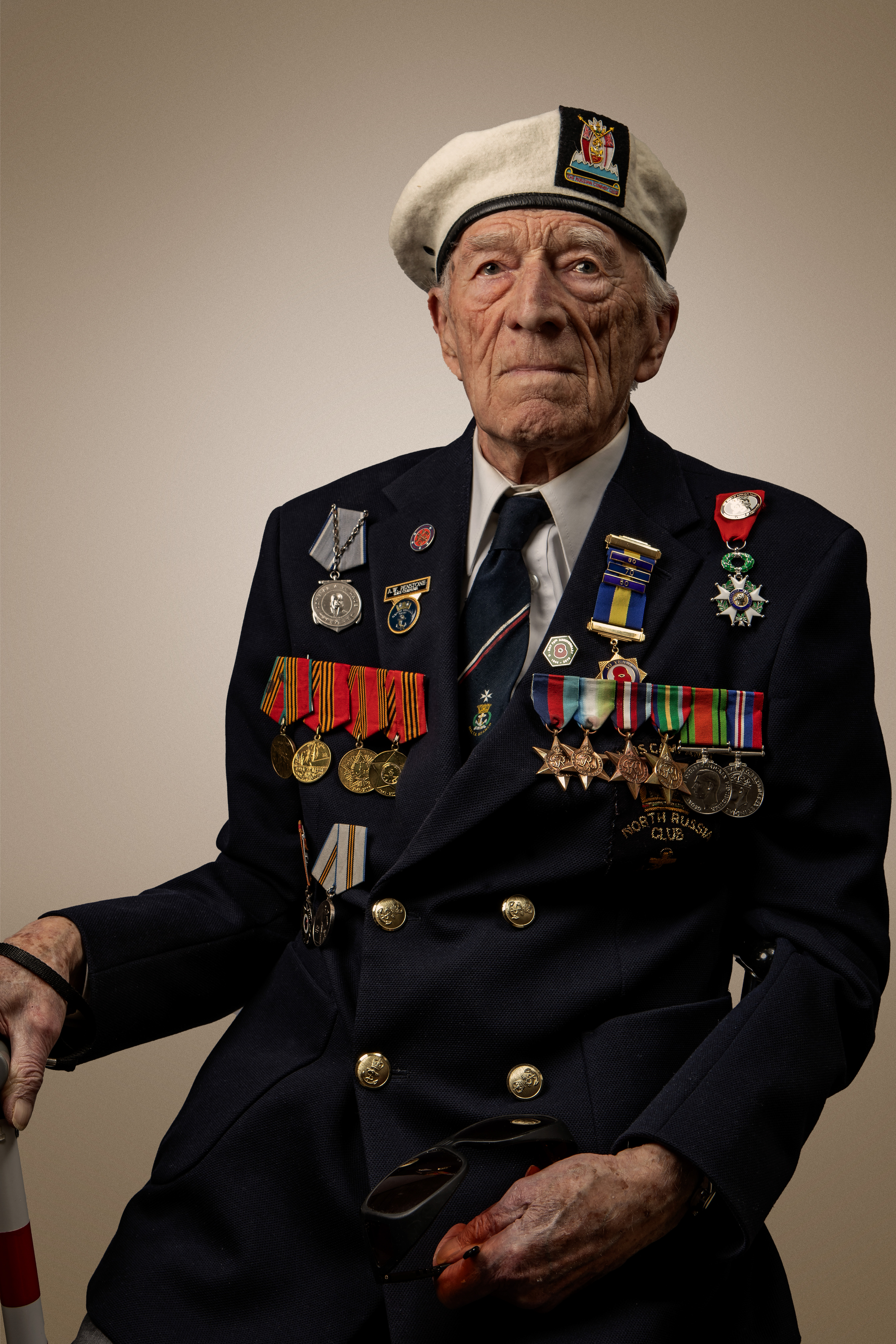 Blind veteran Alec, wearing a suit and his medals sitting in a chain and holding a cane