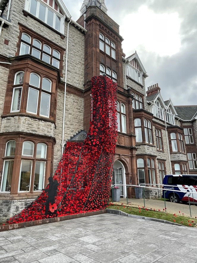 A large poppy blanket, made of up individually knitted poppies, decorating the front entrance of our Llandudno Centre of Wellbeing