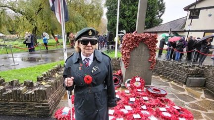 Noeline stood with her white cane in front of the War Memorial with a sea of poppy wreaths at its base