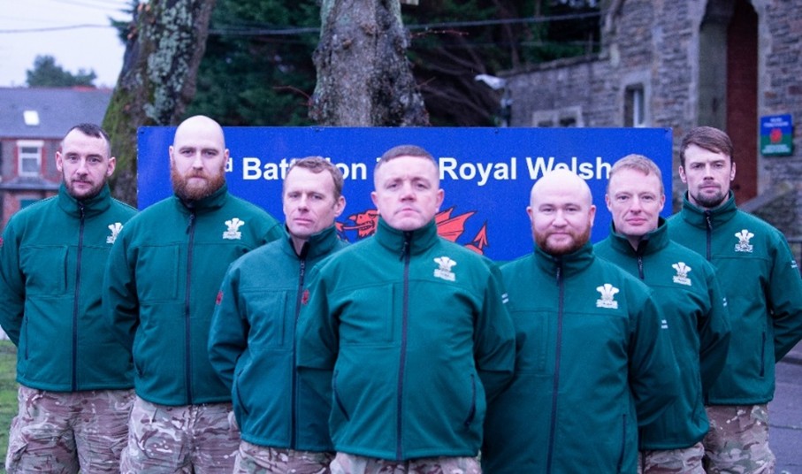Seven soldiers line up in a diamond pattern in front of their regimental branding