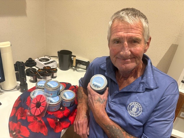 Tony sat down, showing a candle and smiling, while sitting beside a table filled with wax poppies