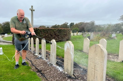 Steve in the Brighton Cemetery using a power washer on the head stones and smiling