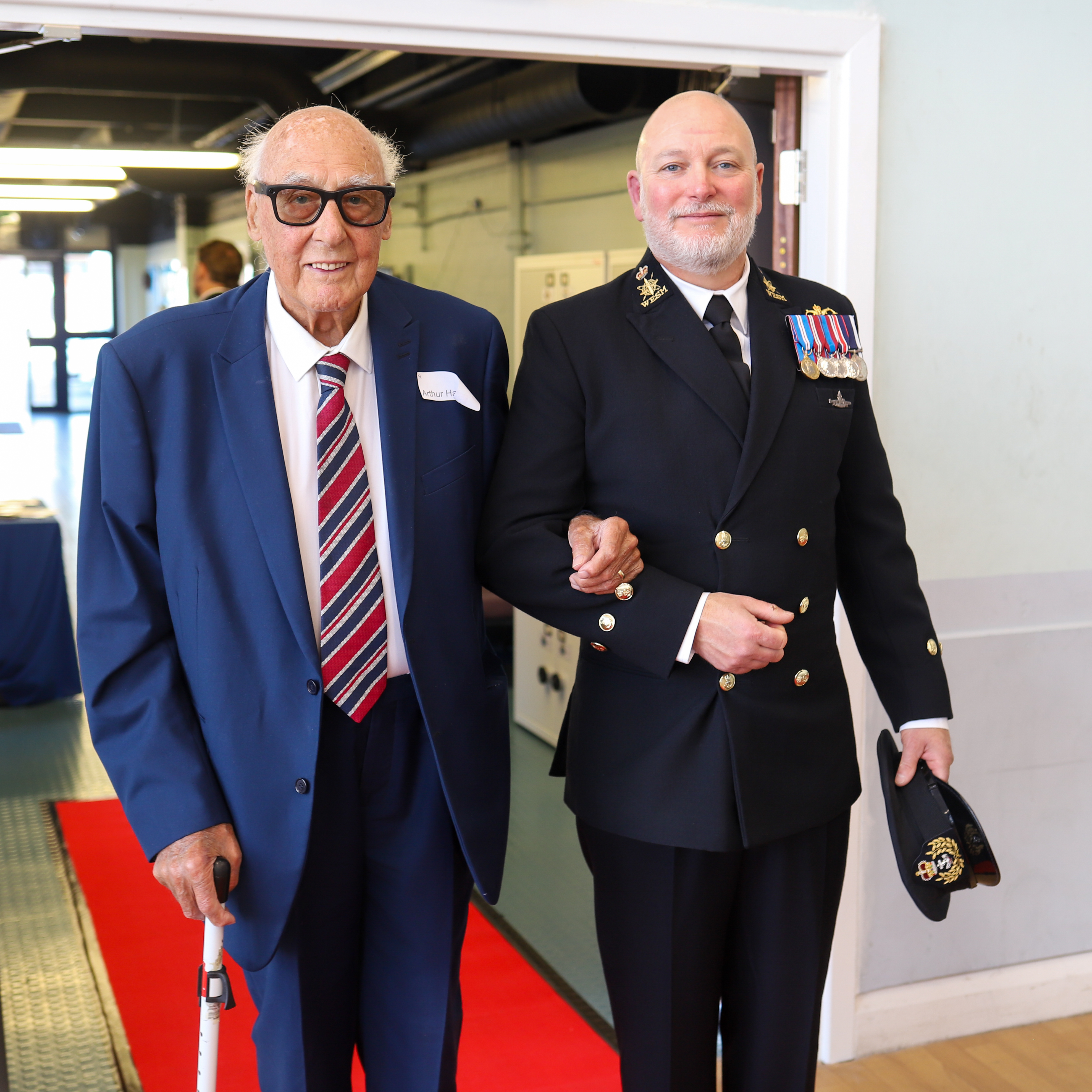 Second World War veteran Arthur (left) being guided down the red carpet by HMS Calliope Commander David A King (right).