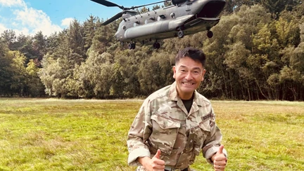 Jim in his Army Cadet uniform stood in a field with both thumbs up with an Army helicopter lifting behind him