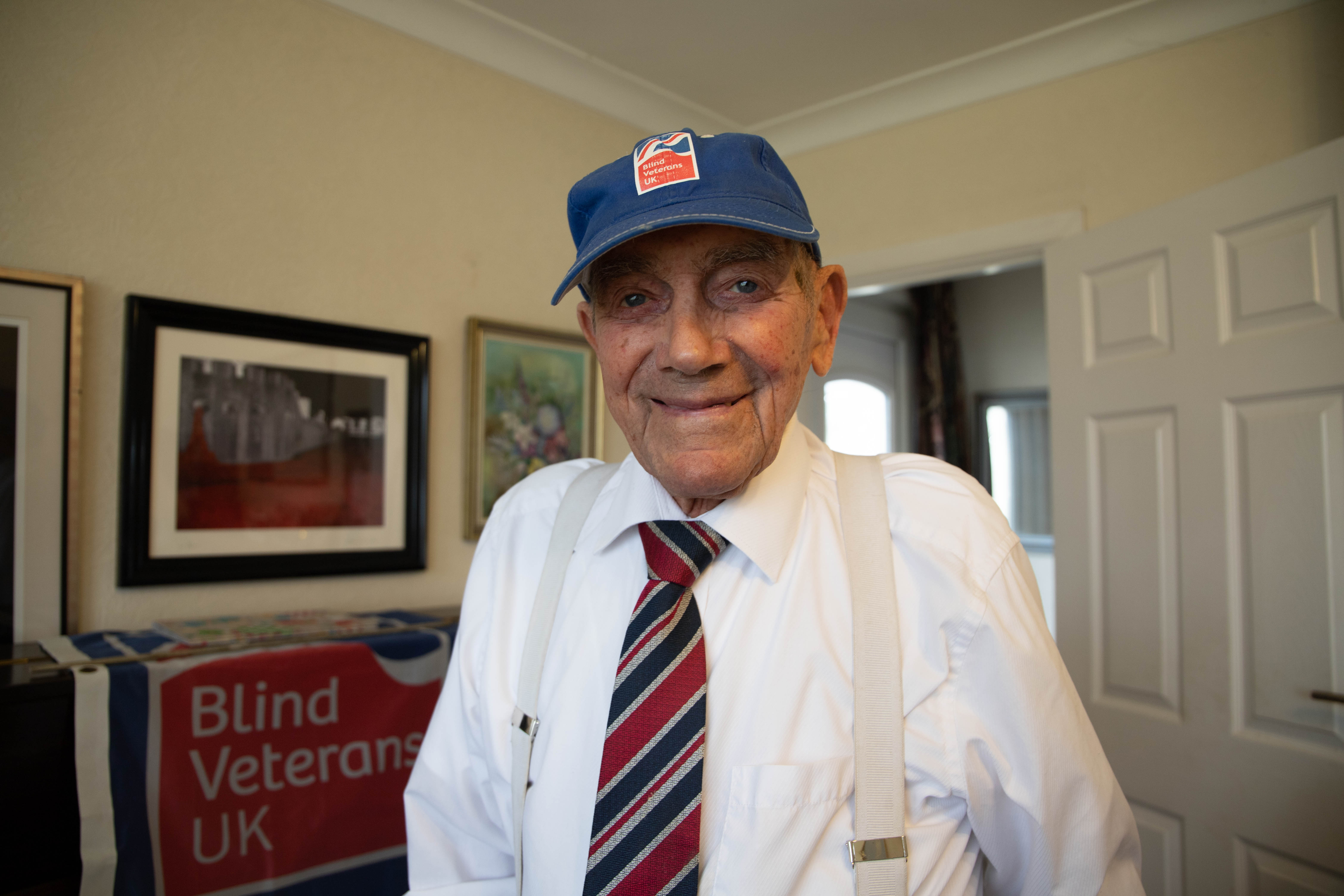 Blind veteran Eddie looking into the camera smiling while wearing a Blind Veterans UK cap and tie