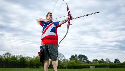 An image of Clive in his GB Archery T-shirt. He stands on the archery field at full draw ready to take his shot