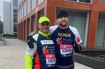 Blind veteran Andy and his guide, smiling, wearing Blind Veterans UK running tops
