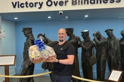 Adam holding his hamper of treats at our Centre of Wellbeing in Llandudno standing in front of the Victory over Blindness statue