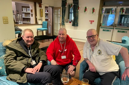 Left to right, Stuart, John, and Jim pictured smiling and sitting down on a sofa and chairs together