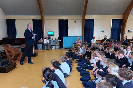 Blind veteran Billy standing in front of a group of pupils and teachers giving a talk in a school hall