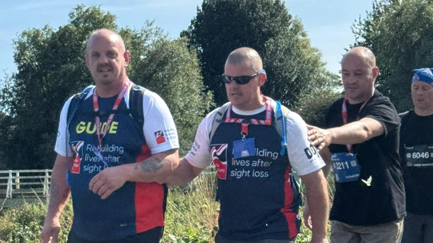 Stu holding on to the arm of Dave as they make there way along with additional support from volunteers behind him