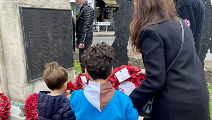 Francesca guides her two young sons towards the war memorial to lay their wreath. One of her sons wears his beaver uniform.