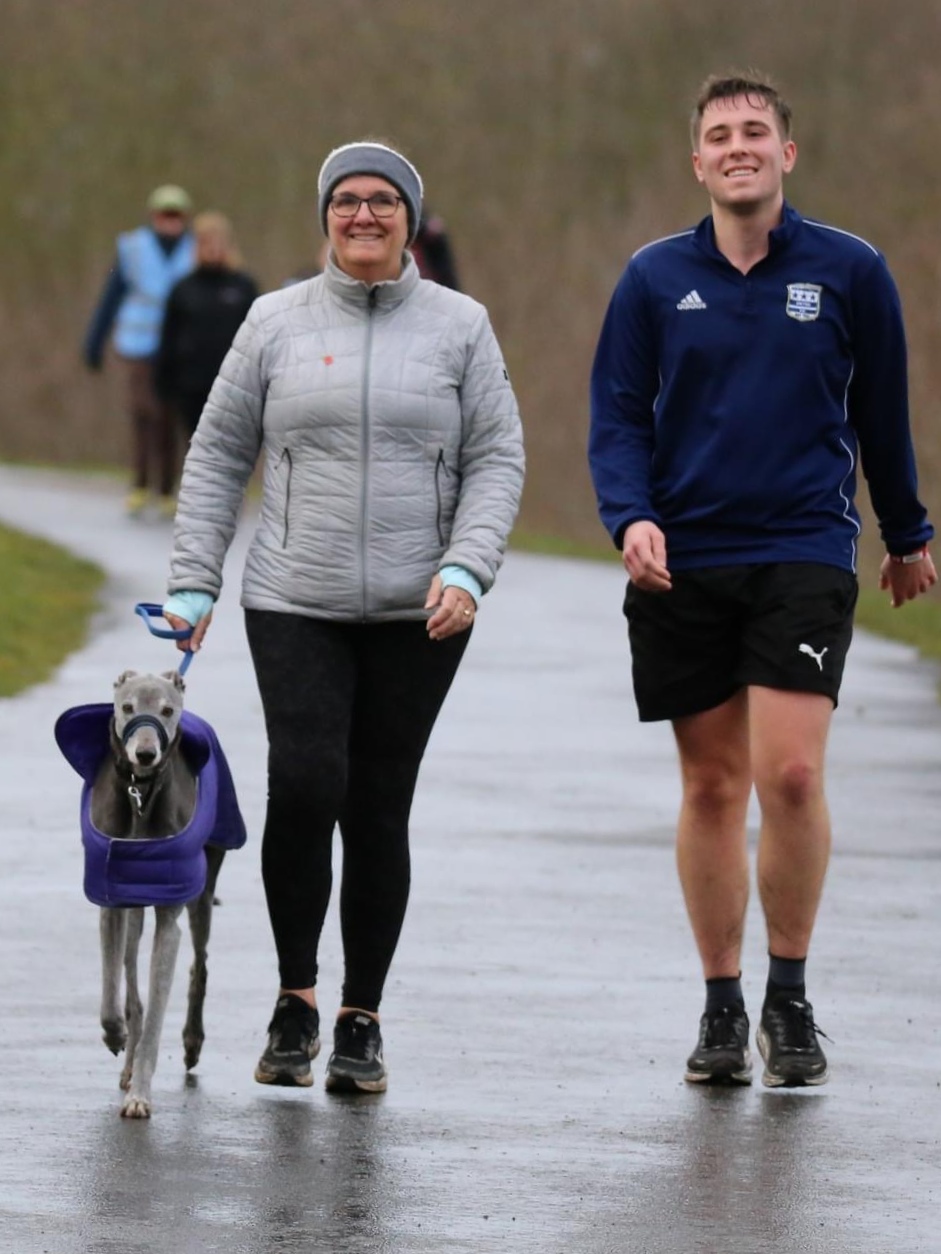 Alison walking in the rain along a tarmac path with her Son Ryan and her dog