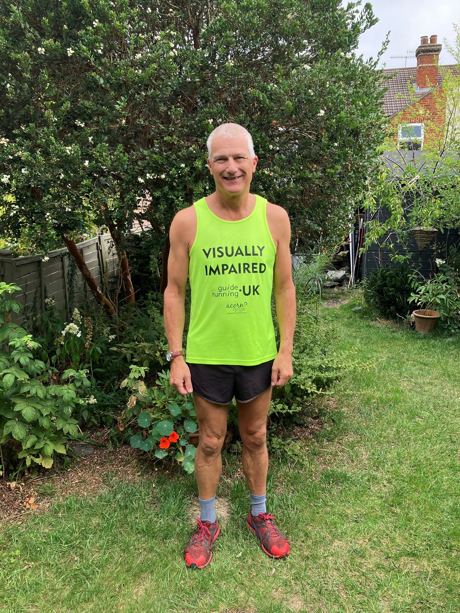 Chris stood in his garden wearing a bright yellow running vest that says 'Visually impaired'