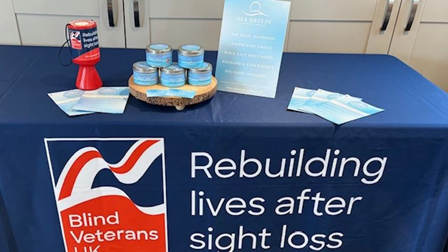 A table with a pyramid of Tony's candles, leaflets about the candles and a Blind Veterans UK collection tin. The table is covered with a Blind Veterans UK cloth.
