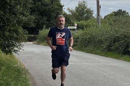 Matt is running along a country road wearing his Blind Veterans UK t-shirt