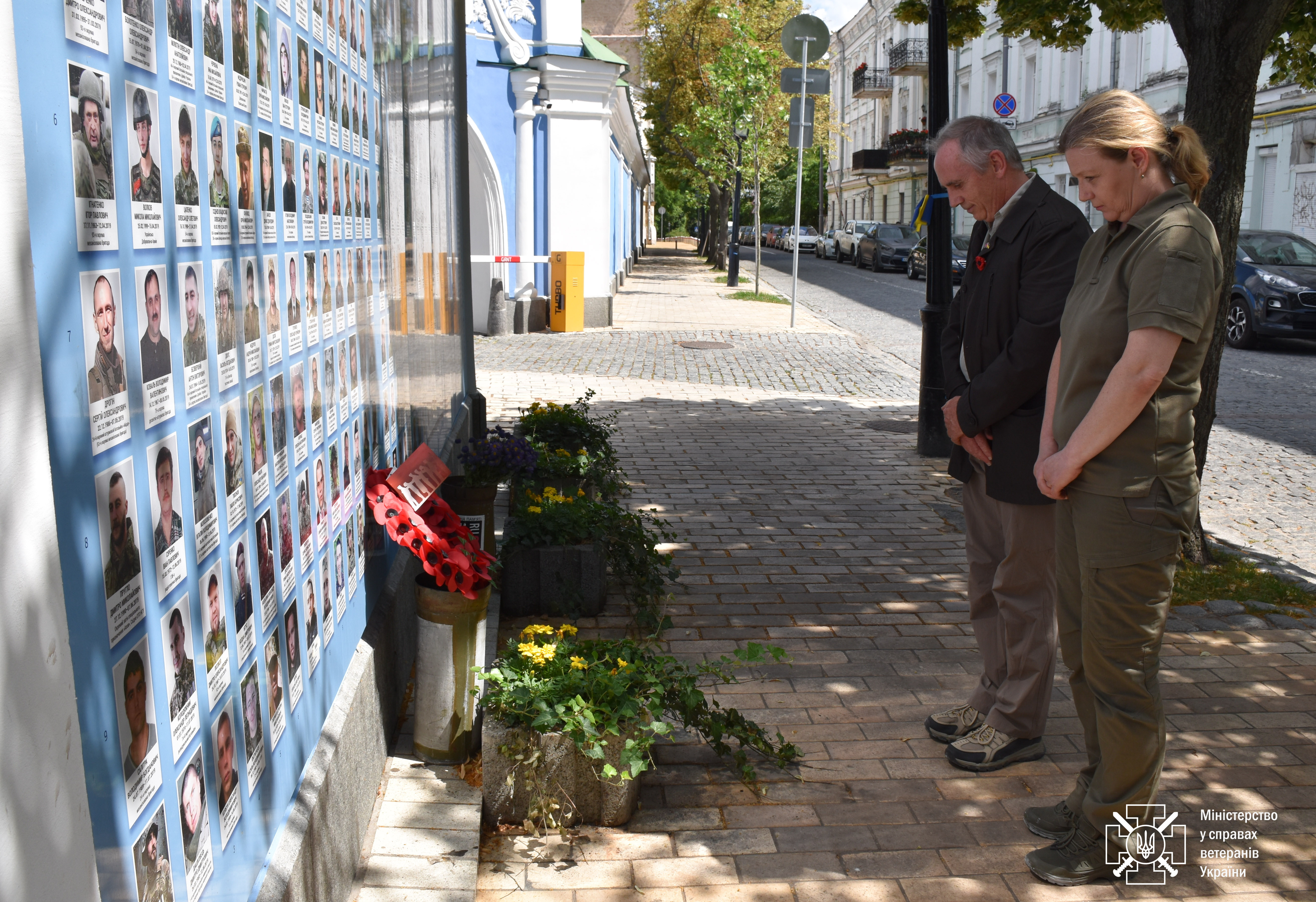 Nick Caplin, stood next to Major General Yulia Laputina, standing with heads bowed at the Borodyanka Memorial, where they stand in front of images of Ukrainian soldiers and memorial wreaths