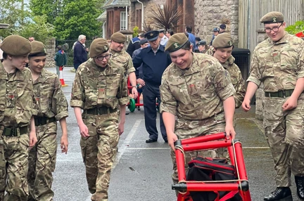 Army cadets smiling and laughing while looking at something they have built made of red plastic poles