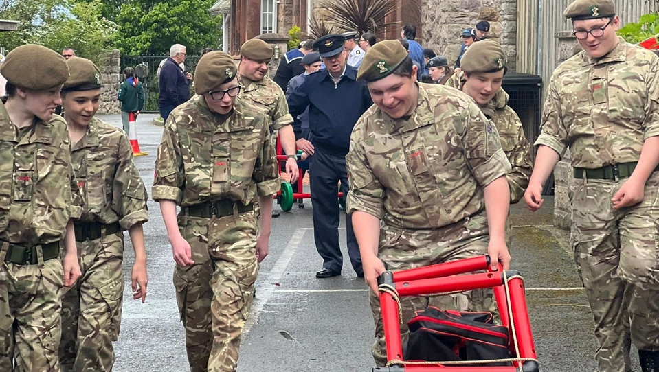 Army cadets smiling and laughing while looking at something they have built made of red plastic poles