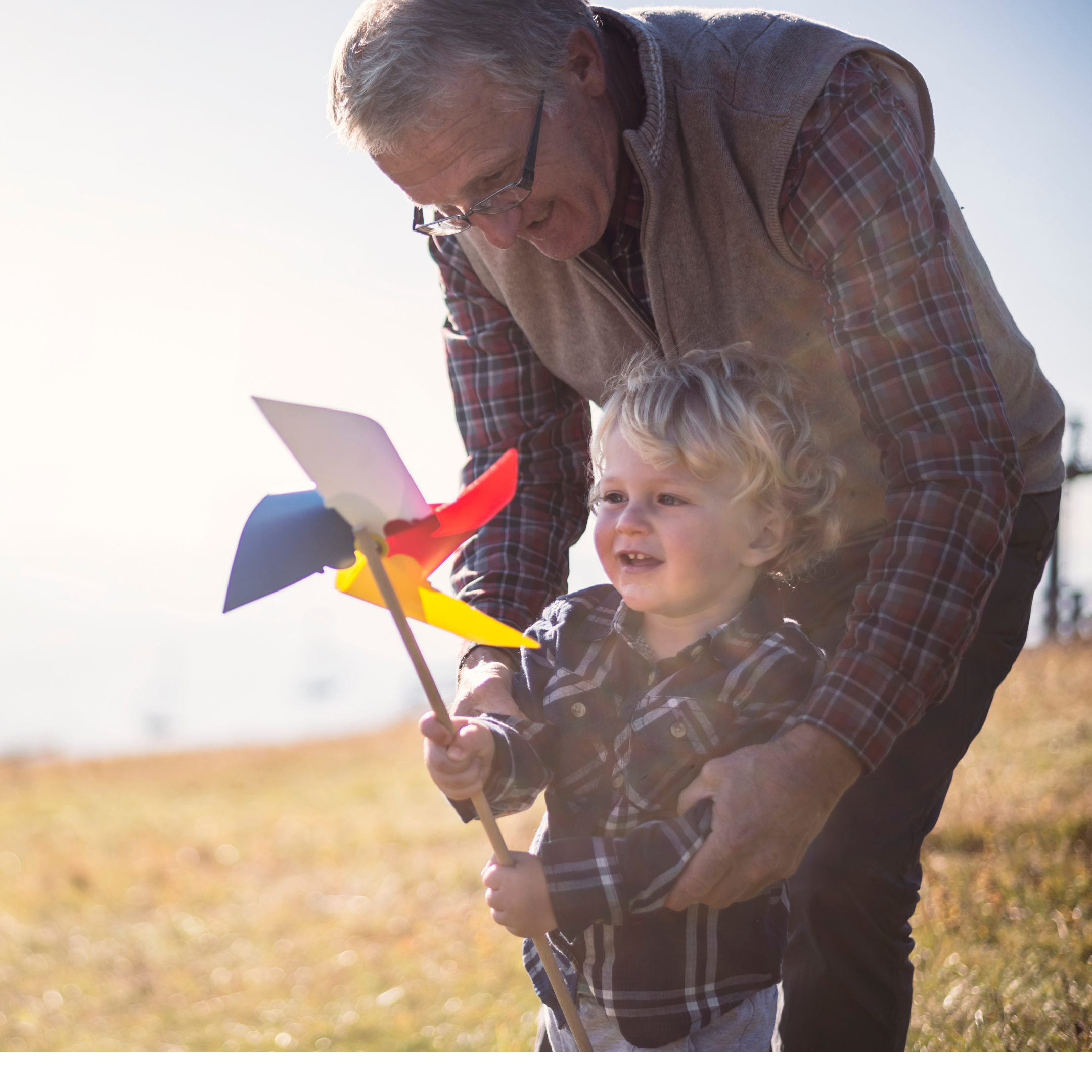 A grandad leaning over his grandson as he plays with a windmill toy