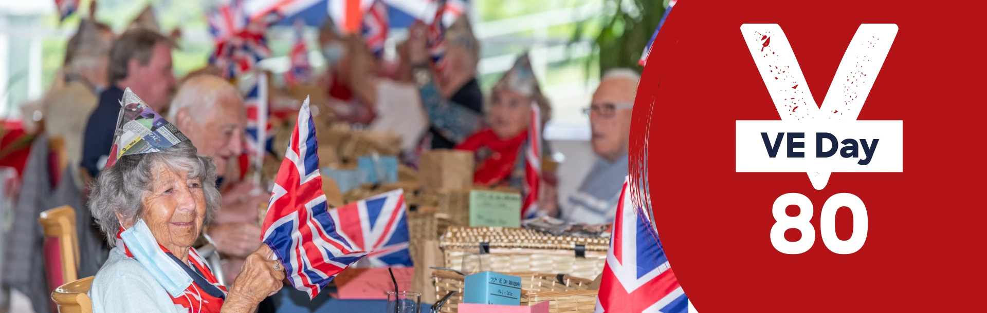 A photo of blind veterans at a VE Day party wearing newspaper hats and waving British flags