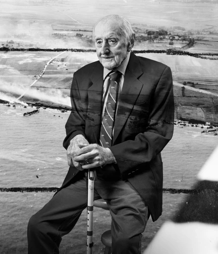 A black and white portrait of D-Day veteran Harry, overlaid on a scene from D-Day