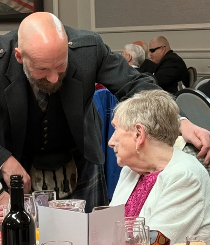 Staff member Scott leaning into congratulate blind veteran Ann