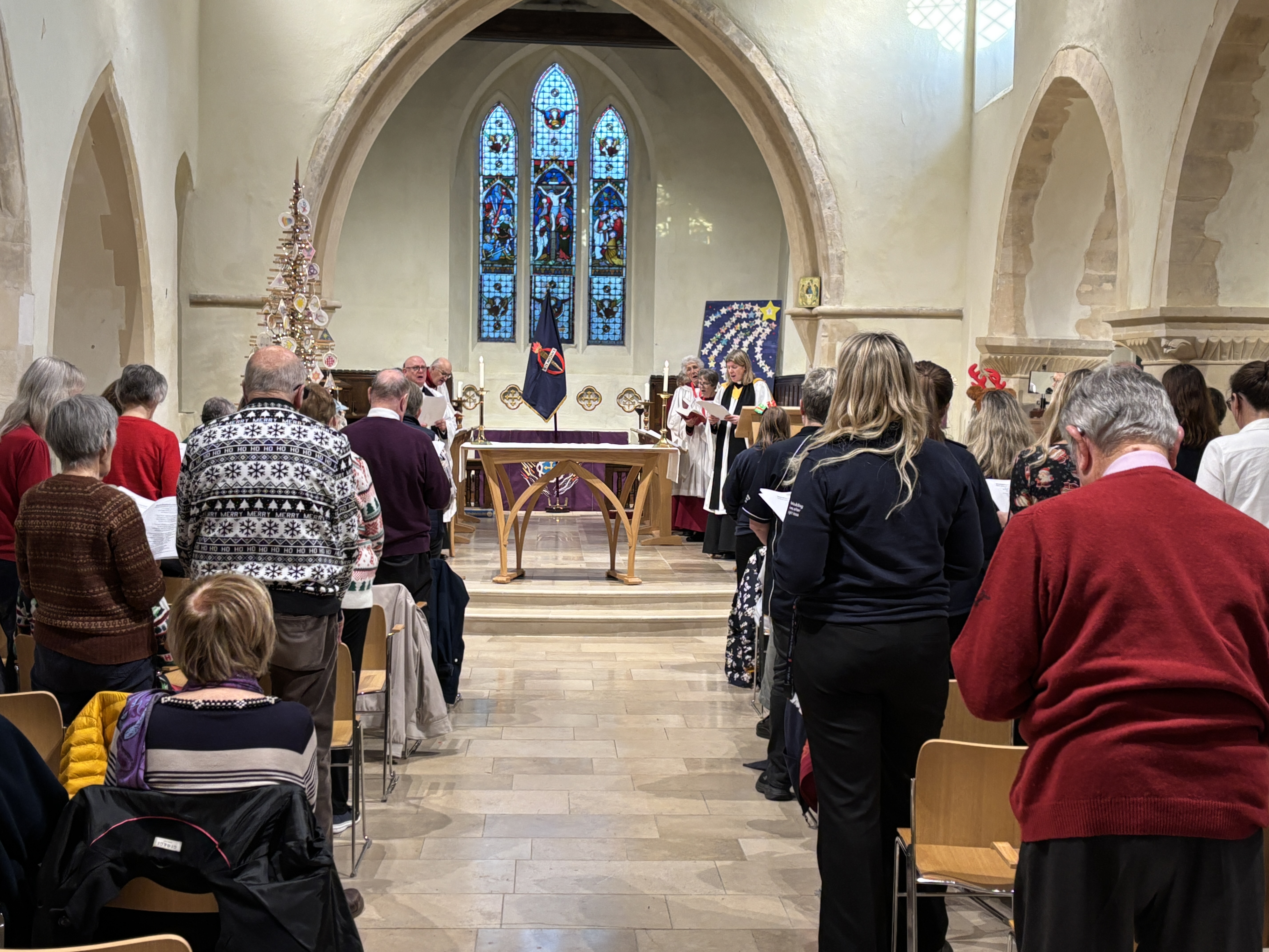 Blind veterans and staff congregate in a church, there is a St Dunstans flag flying at the front