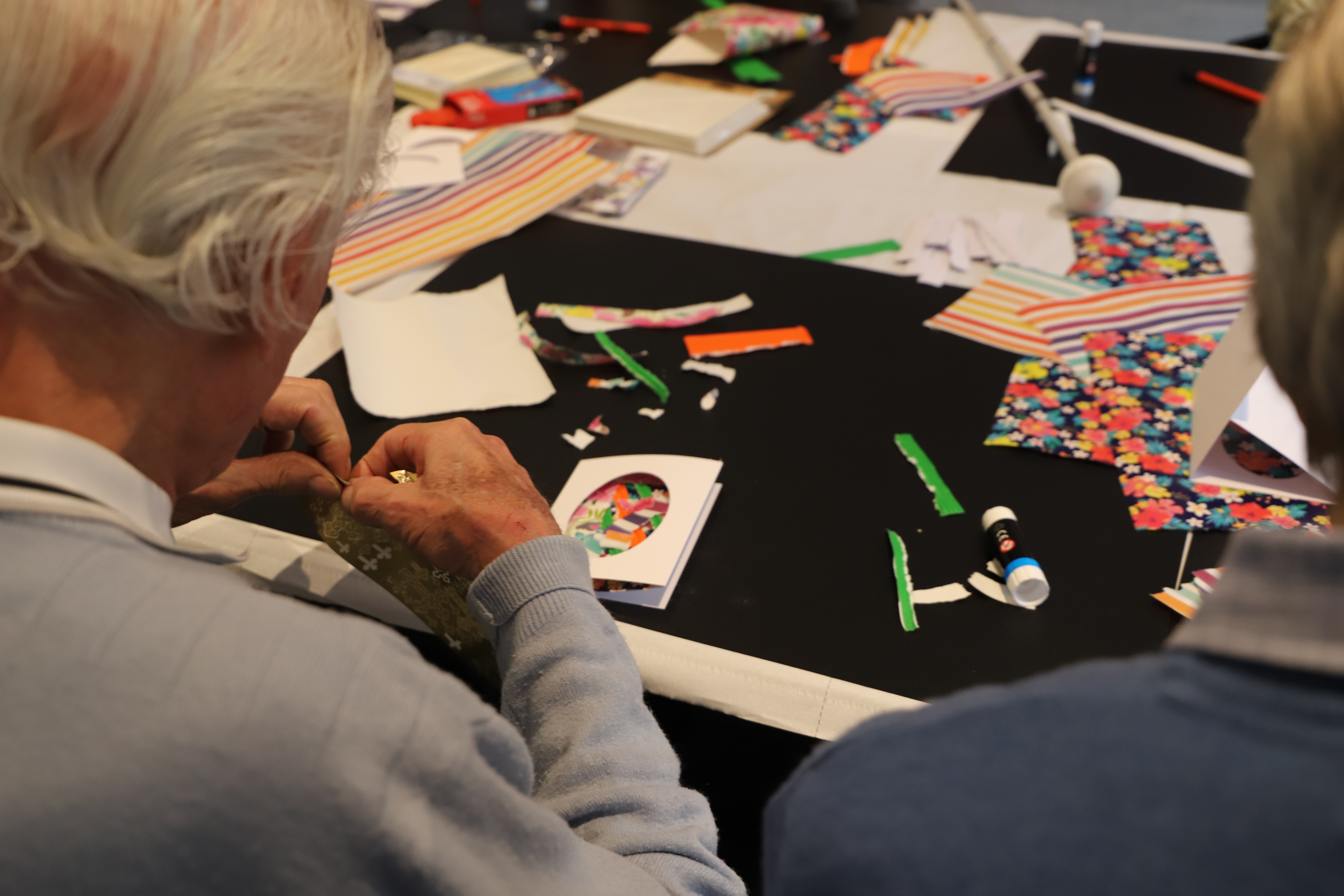 A blind veteran sat a a table sticking decorations onto an Easter themed card 