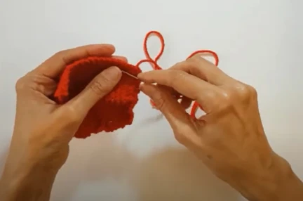 Hands holding a needle and threading a knitted poppy