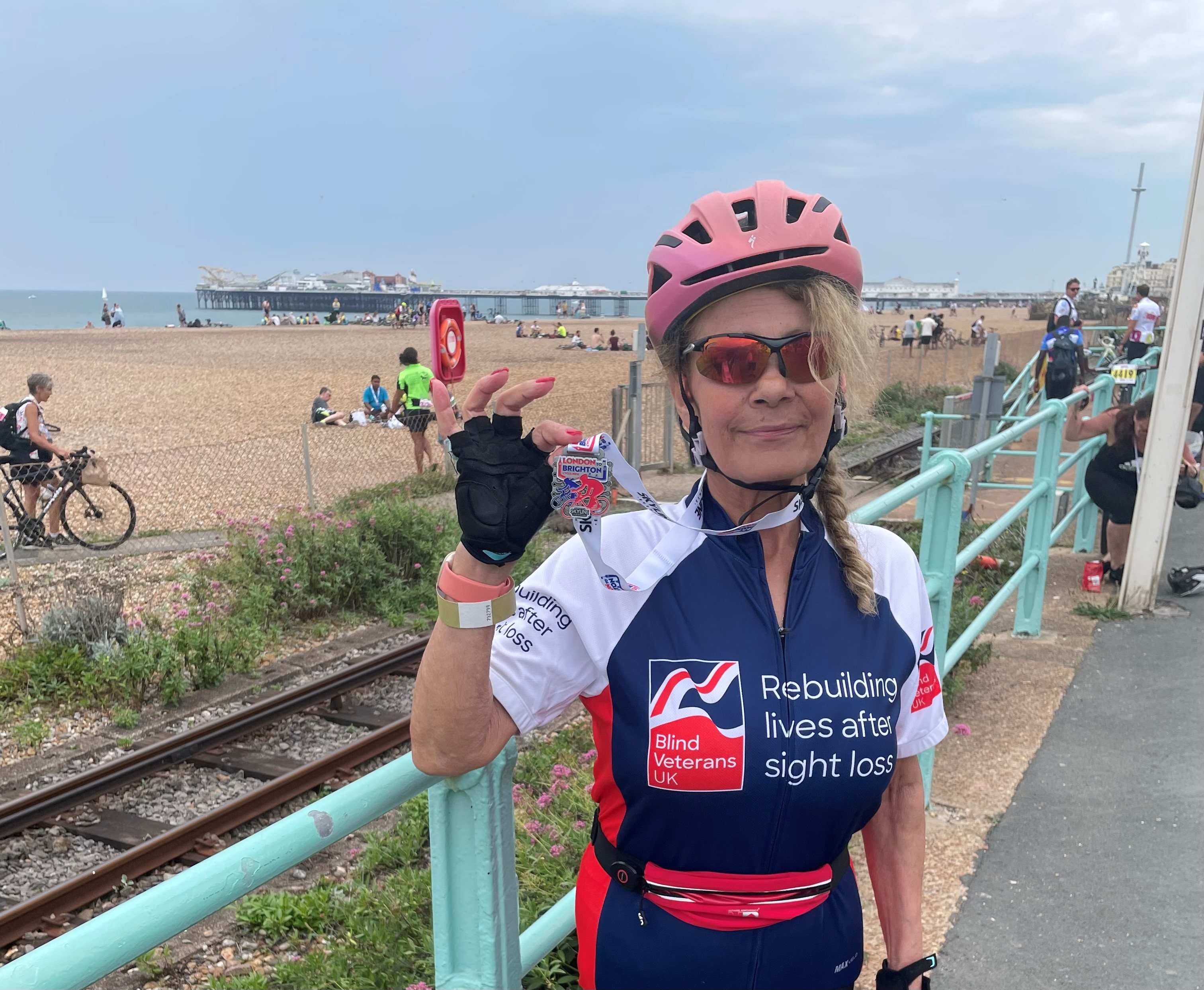 Rider Emilia in her Blind Veterans UK cycling top holding her medal up proudly.  The beach and Brighton Pier can be seen in the background.