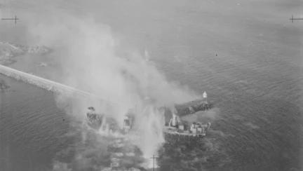 A dramatic scene from D-Day, showing an aircraft smashing into the sea near a ship, emitting a plume of smoke and water.