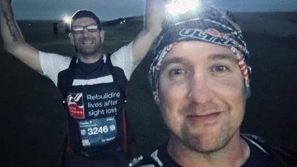 Rich and Charlie are still smiling in the darkness. Rich has a headlamp to help them guide their way and Charlie is in the background with both hands in the air